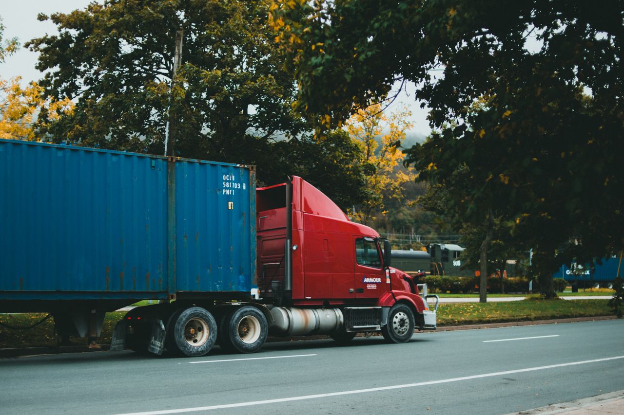 Crafting Captivating Headlines: Your awesome post title goes here A red truck transports a blue cargo container on a scenic, tree-lined road.